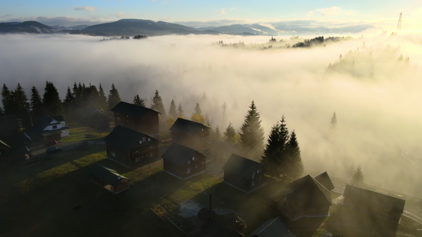 Aerial view of a village houses on hill top in autumn foggy mountains at sunrise.