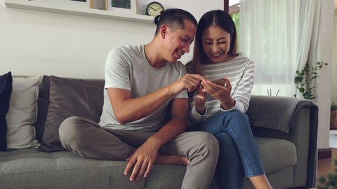 slow motion shot. an Asian Young couple watching online content on a smartphone and shopping online. They sitting on a sofa at home in the living room and play with his dog at home.