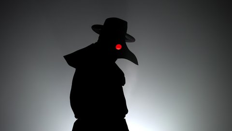 Portrait of plague doctor with crow-like mask and red eyes isolated on black smoke background. Creepy mask, halloween, historical terrible costume concept. Epidemic