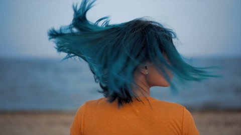 Unusual woman shakes her blue dyed hair on sea beach background. Portrait of hipster girl with unique fashionable hairstyle, she enjoying summertime alone, demonstrate her fresh color.