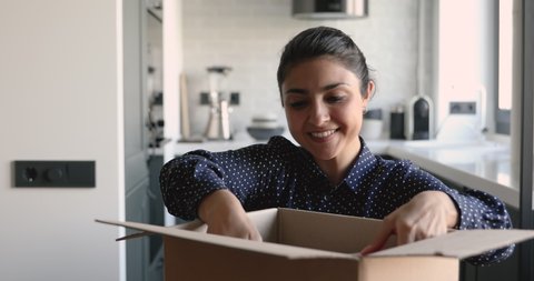 Head shot excited young indian ethnicity woman unpacking huge carton box with belongings, moving in new apartment. Smiling millennial mixed race female client satisfied with online bookstore offer.
