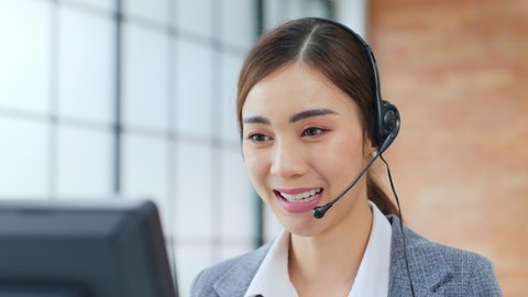 Closeup Asian woman call center, customer service, telesales in formal suit wearing headset or headphone talking with customer in modern office