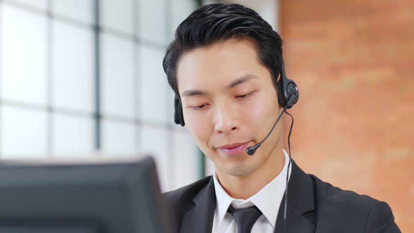 Closeup Asian man call center, customer service, telesales in formal suit wearing headset or headphone talking with customer in modern office | Shutterstock HD Video #1063059343