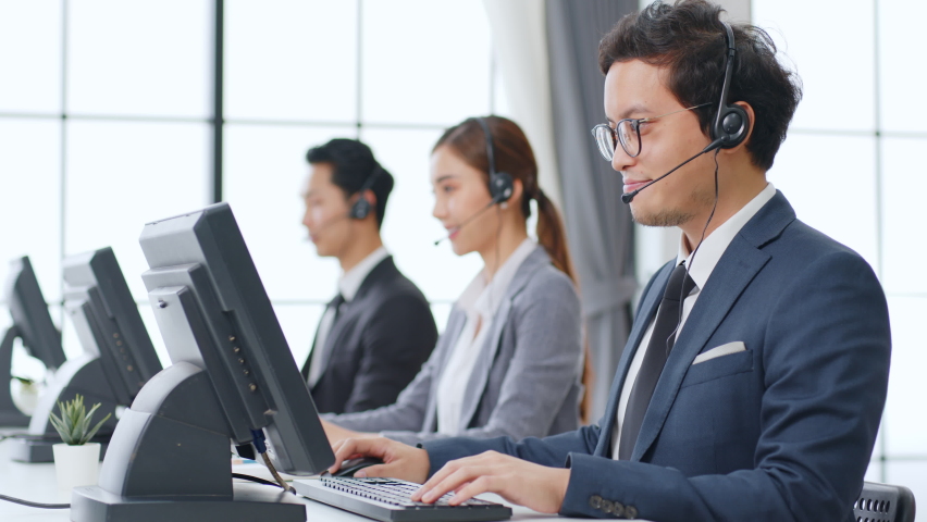 Asian call center team, customer service, telesales in formal suit wearing headset or headphone talking with customer in modern office | Shutterstock HD Video #1063059358