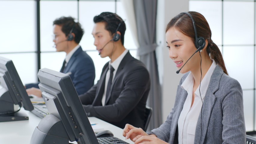 Asian call center team, customer service, telesales in formal suit wearing headset or headphone talking with customer in modern office | Shutterstock HD Video #1063059388