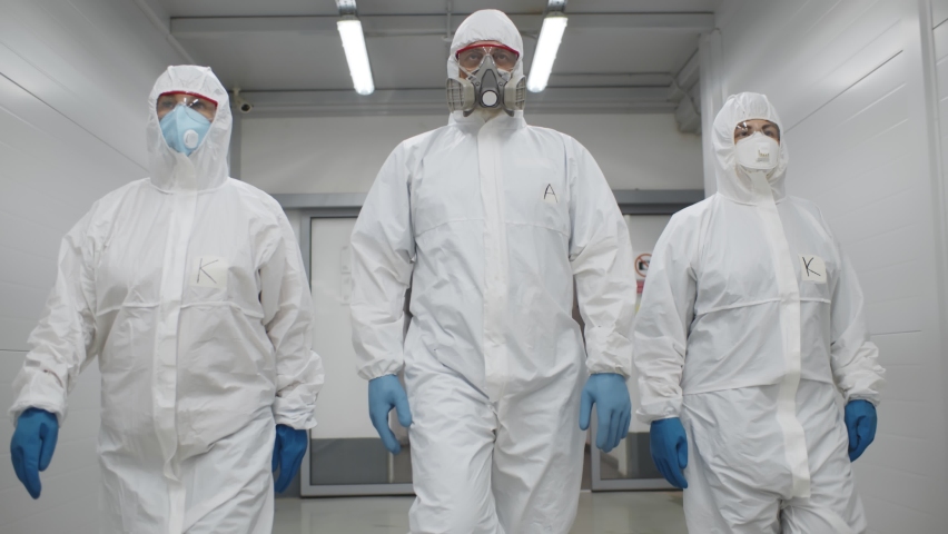 Team of virologists in hazmat suits walking in corridor to do disinfection. Specialists in protective overalls and respiratory mask walking in hallway of industrial building or hospital Royalty-Free Stock Footage #1063059937