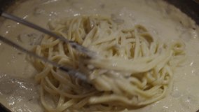 Stirring pasta with  creamy sauce with white mushrooms inside frying pan. Slow motion shot. Cooking creamy pasta. Close up shot.