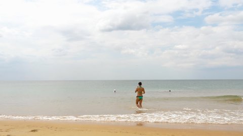 A Woman in a bikini swimsuit is shooting a video walking in the shallow water of the beach. Mai Khao beach, Phuket island.