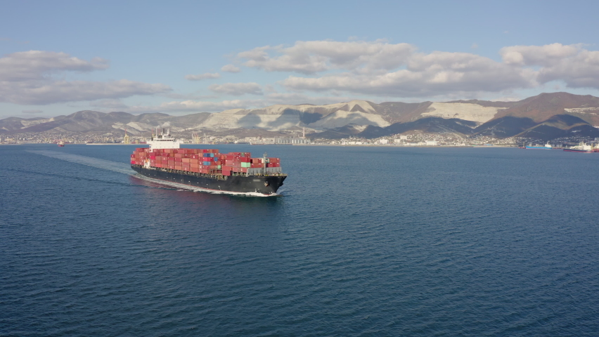 Aerial footage of ultra large container ship at sea, side view. Cargo ship with colourful containers leaves port in sunny weather. Following drone 4k footage sea port at background | Shutterstock HD Video #1063069618