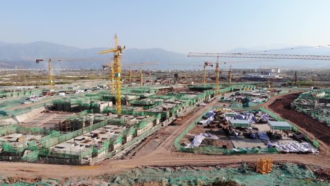 XICHANG,CHINA SEP 2020: Flying towards huge Chinese residential apartment construction site. Drone aerial view of new development with cityscape in background. Rising up for a wide view of building w