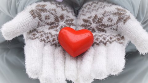 Close-up of female hands in warm winter gloves holding decorative heart, selective focus. The concept of Valentines Day.
