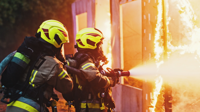 Close up, two firefighters extinguish fire, spraying house with hose at night. High quality 4k footage Royalty-Free Stock Footage #1063077214