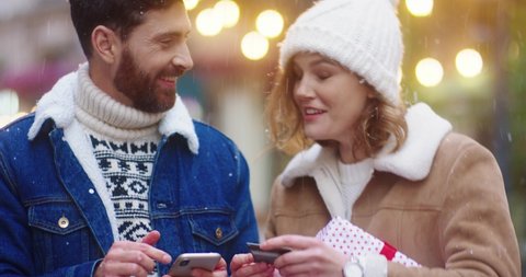 Young happy caucasian couple shopping online using mobile phone and bank card standing on street. Happy woman hugs her husband.