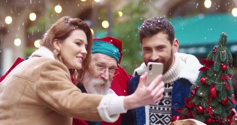 Happy Caucasian young couple making joint photo on smartphone with Santa Claus standing in the city center. Holiday mood.