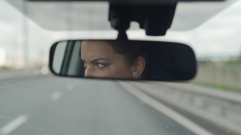 Brunette woman sitting behind the wheel driving car female driver face in rear view mirror closeup.