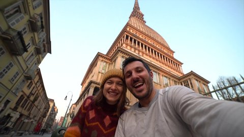 Young female and man couple tourist standing on the famous cityscape with Mole Antonelliana in Turin (torino) city. Travelling in Europe, Piedmont region in Italy. slow motion video