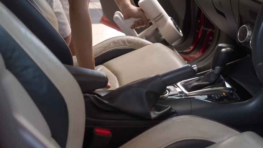 Asian man using handheld vacuum cleaning dust from passenger front seat of luxury car. | Shutterstock HD Video #1063082845