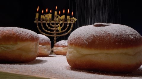 Sufganiyot are fried balls of yeast dough filled with strawberry jelly and dusted heavily with powdered sugar. The Hanukkah menorah and lights. Cooking of doughnuts 