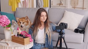 An Attractive Teenage Girl with Her Cute Dog Vlogs While Doing Makeup. A Young Girl Conducts Distance Learning in Makeup, Skin Care, While Blogging. showing glamour look. Next Generation of Beauty Influencers.