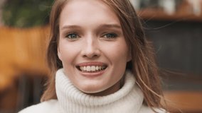 Portrait of pretty smiling girl dressed in cozy white sweater looking happy posing on camera outdoor