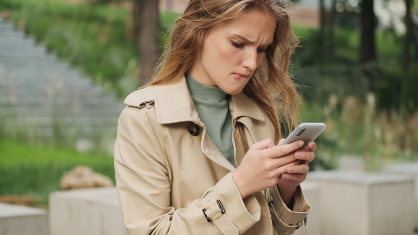 Attractive student girl biting lip looking worry while texting with classmates in chat using smartphone outdoor