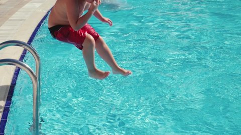 Fullness kid jumping in pool and splashing crystal clear water in basin at sunny day. Boy relaxing during summer vacation, slow motion