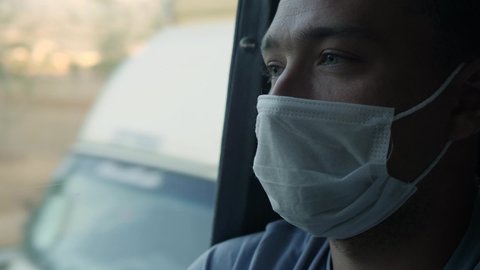 Middle-aged green-eyed man in protective face mask looks out the window on a bus ride. Travel safety during coronavirus pandemic quarantine concept
