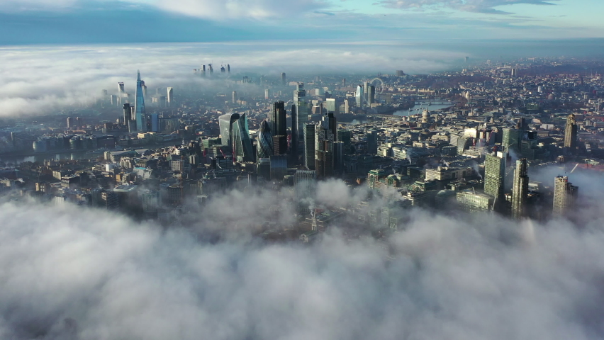 London, United Kingdom, 28-11-2020: Aerial Drone Helicopter London City above the clouds and fog, The Shard Skyline, Thames River, London Eye, The Gherkin, Cityscape and Iconic commercial Skyscrapers