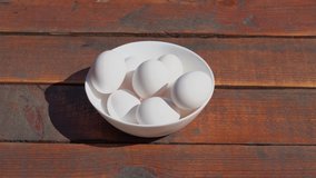 Closeup view of white bowl full of fresh white chicken eggs isolated on wooden brown background.