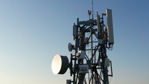 Silhouette of a communication tower for 5G network featuring cellular microwave wireless directional antenna of radio relay link used for mobile telecommunication.