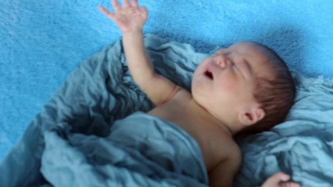 Newborn crying baby boy. New born child tired and hungry in bed under blue knitted blanket. Children cry. Bedding for kids. Infant screaming. Healthy little kid shortly after birth.