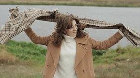 A beautiful young woman stands on the background of the river and puts a scarf on her neck wrapping herself in a coat and closes her eyes. Slow motion - Powered by Shutterstock - Get 15% off with code: PIKWIZARD15