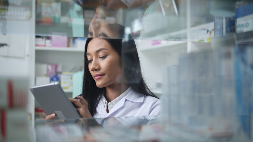 Asian pharmacists working and checking drug in pharmacy store at hospital. Asian doctor checking medicine cabinet and wearing white medical coat. Shelves pharmacy background in drugstore. | Shutterstock HD Video #1063104916