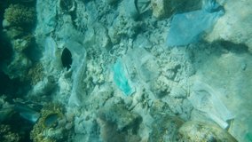 VERTICAL VIDEO: Face masks, plastic and other debris of the coral reef on bottom, tropical fish swim over this garbage. Plastic garbage on coral seabed. Plastic pollution of the Ocean.
