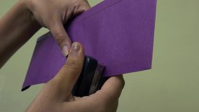 Asian female hand stapling on purple paper isolated on cream color background.