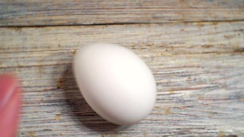 white chicken egg rotates on a wooden surface. close-up. view from above