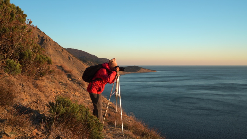 Female photographer takes pictures with a tripod at sunset in the highlands on the coast. Mountains on the Black Sea coast.