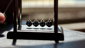 Hand putting a simple Newtons cradle in motion in sunlight, macro, closeup. Metal balls swinging and slowing down. Moving something, inertia concept, science, fun physics lesson toy, real time - Powered by Shutterstock - Get 15% off with code: PIKWIZARD15