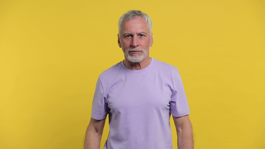 Cheerful funny elderly gray-haired mustache bearded man in casual violet t-shirt isolated on yellow color background studio. People lifestyle concept. Dancing clenching fists waving clapping hands Royalty-Free Stock Footage #1063109149