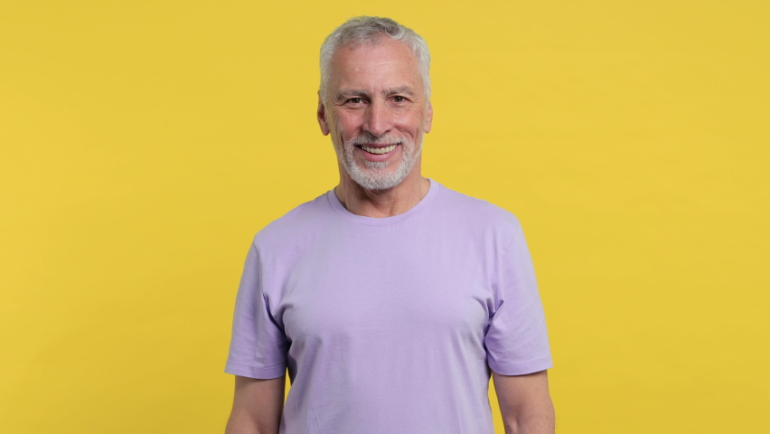 Smiling cheerful laughing elderly gray-haired mustache bearded man in casual violet t-shirt isolated on yellow color background studio. People sincere emotions lifestyle concept. Looking camera aside Royalty-Free Stock Footage #1063109269