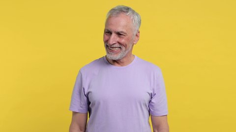 Smiling cheerful laughing elderly gray-haired mustache bearded man in casual violet t-shirt isolated on yellow color background studio. People sincere emotions lifestyle concept. Looking camera aside