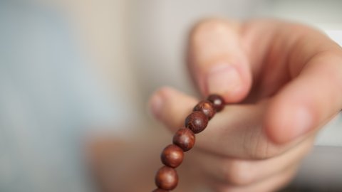 A man's hand with a wooden rosary, goes through a rosary, blurred background, close-up