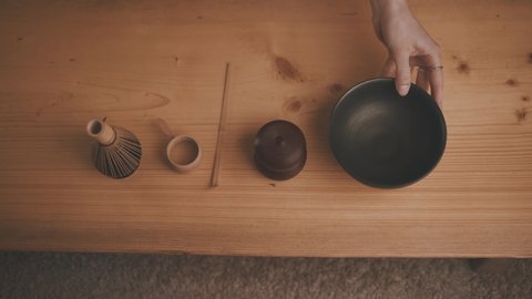Female hands lay out Tools for traditional brewing of matcha tea: BAMBOO CHAISEN WHEEL, tea sieve, tea jar, SPOON CHASAKU TYAVAN bowl on wooden table background. Flat lay top view ceremony preparation