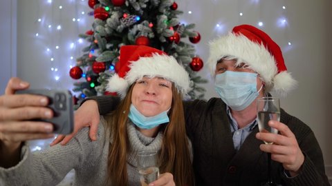 Couple, young family wearing masks. Communicate online with family. Decorated bright Christmas tree with lights. Merry christmas coronavirus pandemic