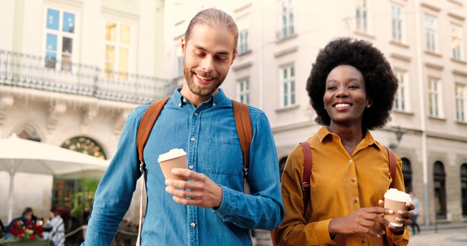 Close up portrait of mixed-races friends standing in city and making selfie photos on smartphone on sunny day. Joyful Caucasian guy taking pictures on street with women and African American female