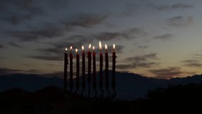 4 K video with burning flames of candles on menorah - symbol of Jewish holiday of light, background with dramatic sky above mountains