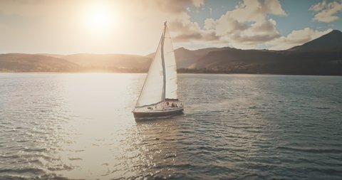 Luxury yacht race at sun light aerial. Yachting on serene seascape at open sea. Boat with big white spinnaker sail at ocean bay. Lonely ship cruise at water on summer sunny day. Cinematic drone shot