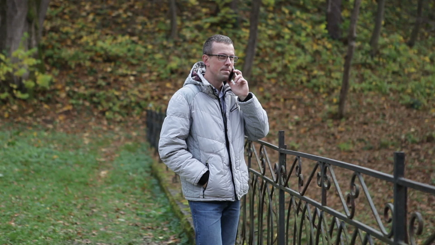 A man in a city park talking on a cell phone.
