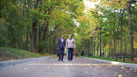 Mature couple walking in park on autumn day. Full length portrait of happy senior couple walking together in a city park. Mature man and woman On a walk
