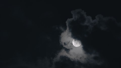 Full moon on dark cloudy night. Clouds passing by the moon in spooky feeling like thriller and horror films. Werewolf moon, dark night sky, black clouds, full moon clouds, ghost, horror films.
